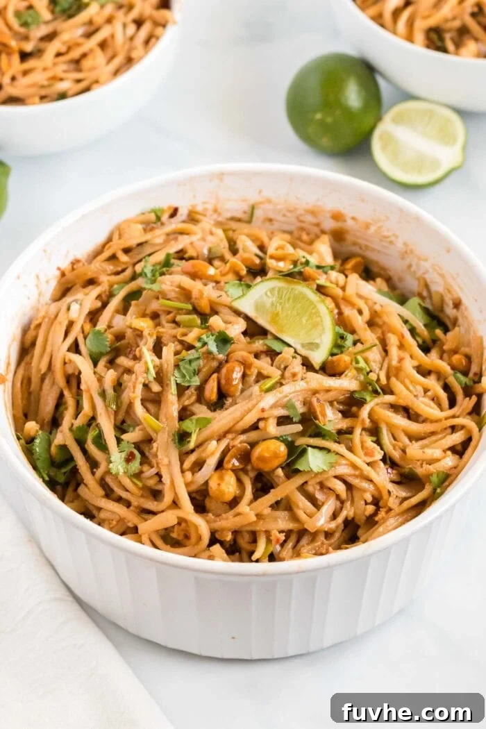 A beautifully presented serving bowl of vegan tofu Pad Thai, generously topped with a sprinkle of crushed roasted peanuts, fresh green cilantro, and a bright yellow lime wedge, ready to be enjoyed.