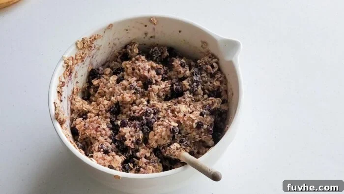 Superfood Quinoa Energy Bars 7 Thick batter with blueberries in it in a large mixing bowl with a spoon resting in it.