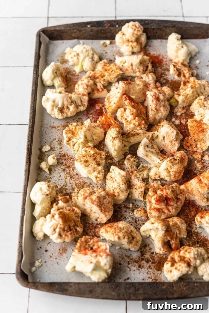 Chopped cauliflower coated in vibrant spices on a baking tray, ready for roasting.