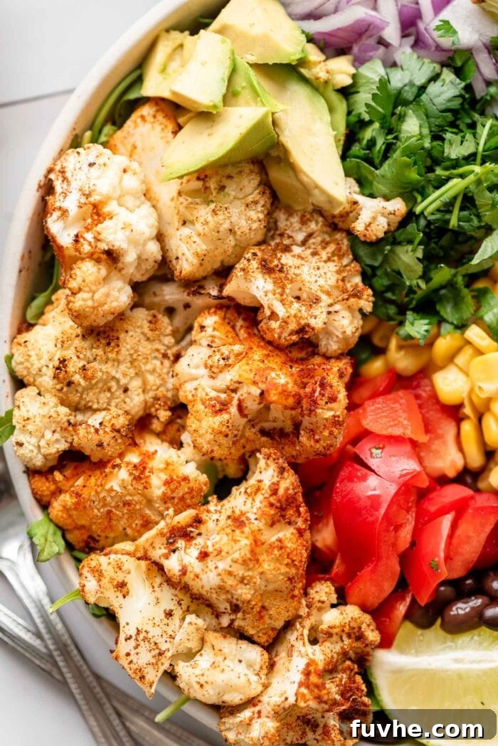 A close-up view of a roasted cauliflower burrito bowl featuring vibrant avocado, colorful bell pepper strips, and fresh cilantro, highlighting the dish's fresh ingredients.