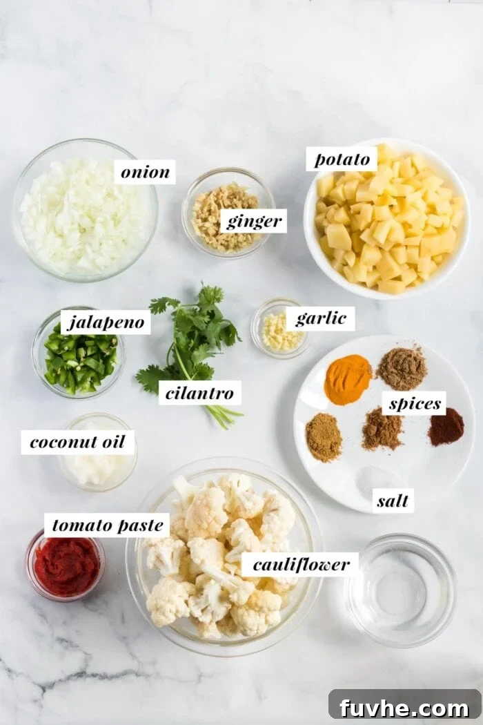 Comforting Cauliflower Potato Curry 3 A visual display of fresh ingredients laid out, including onions, garlic, ginger, jalapeno, turmeric, cumin, coriander, garam masala, chili powder, potatoes, and cauliflower, ready for an aloo gobi curry.