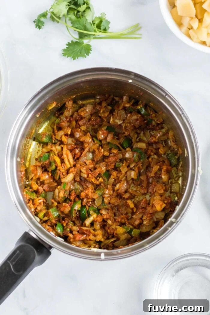 Comforting Cauliflower Potato Curry 5 The pan now contains the softened onion, garlic, ginger, and jalapeño, generously coated in a vibrant blend of turmeric, cumin, coriander, garam masala, chili powder, and a dollop of tomato paste, creating a rich spice paste.