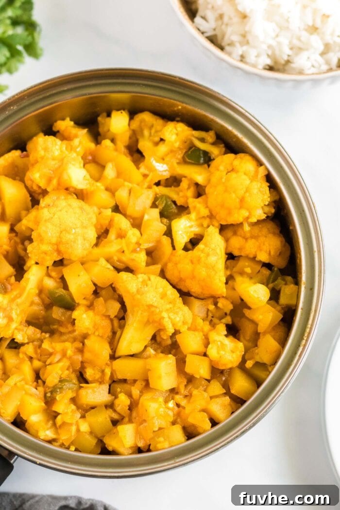 Comforting Cauliflower Potato Curry 8 A pot filled with golden curried potatoes and cauliflower, simmering gently, with steam rising, indicating the final stage of cooking.