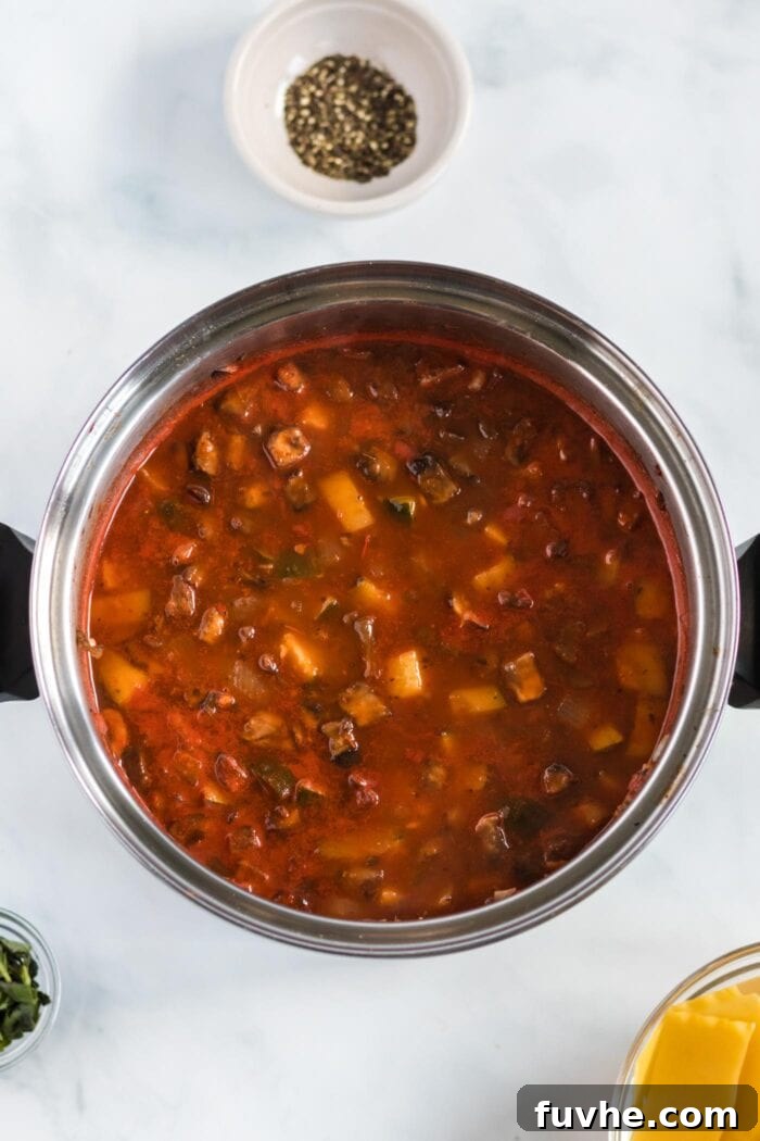 Crushed tomatoes and vegetable broth simmering in a large pot with the sautéed vegetables and herbs, developing into a rich soup base.