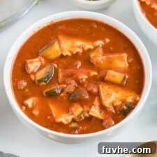 A beautifully presented bowl of vegan lasagna soup, garnished with fresh basil, cracked black pepper, and a creamy swirl of tofu ricotta.