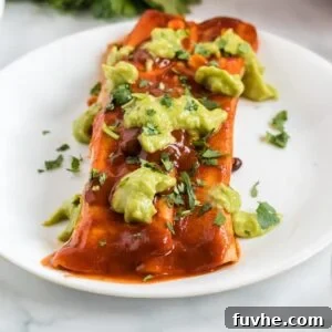 Close up of an enchilada topped with guacamole on a plate.