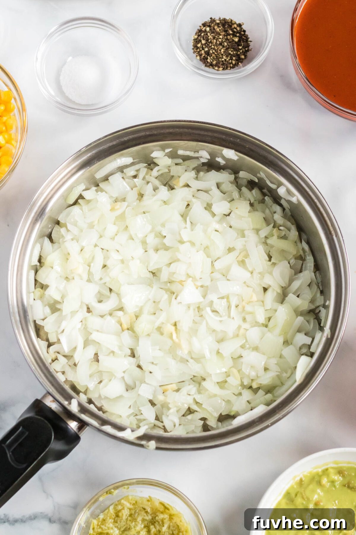 Diced white onions and minced garlic cooking in olive oil in a large silver frying pan over medium heat, releasing their aromatic flavors.