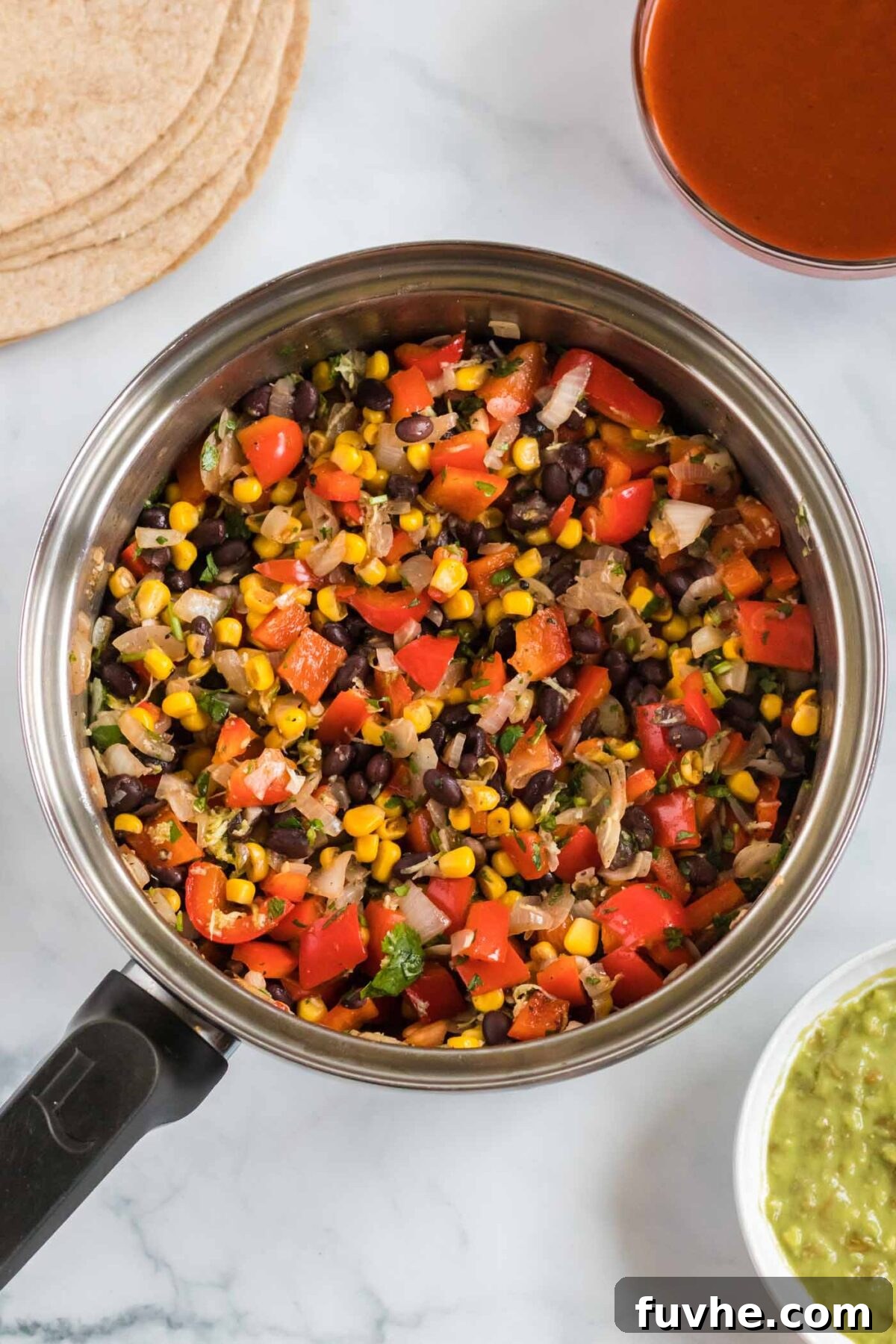 A vibrant mix of corn kernels, diced bell peppers, and black beans actively cooking in a large skillet, releasing steam and mingling flavors.