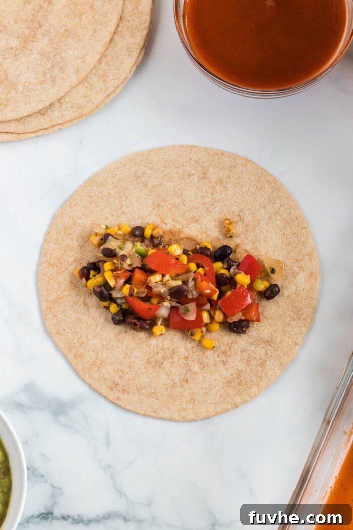 A single wheat tortilla topped with a generous scoop of black bean, bell pepper, and corn filling, perfectly portioned for rolling into an enchilada.