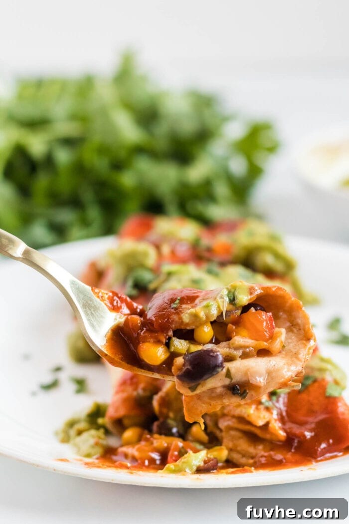 A fork piercing into a delicious black bean and corn enchilada, showcasing its hearty filling and the soft, saucy tortilla.