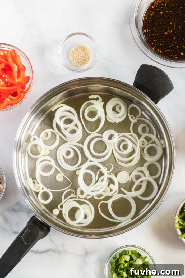 Sliced onions cooking in a large frying pan, lightly caramelized and softened.