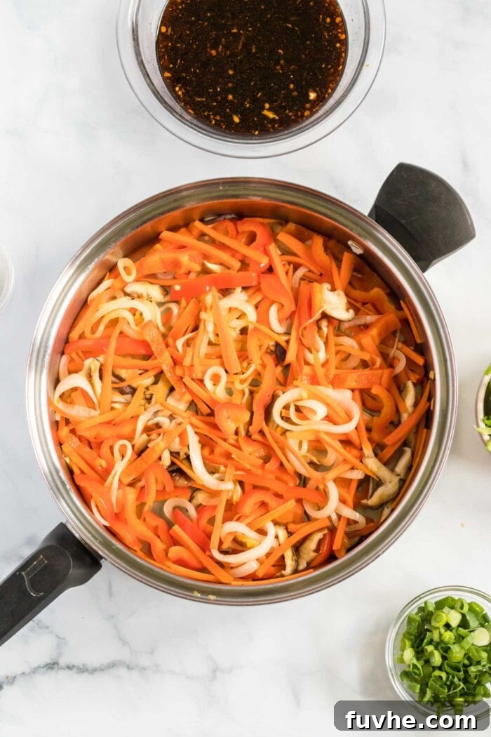 Carrots and onions cooking together in a large frying pan, bright and tender-crisp.