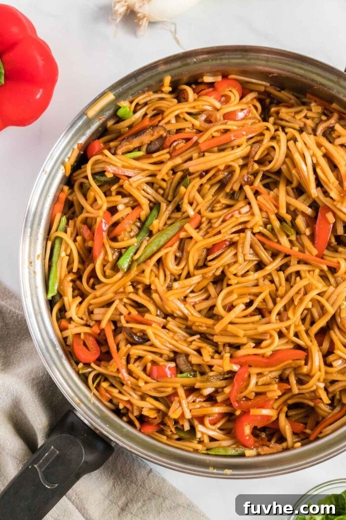 Rice noodles perfectly coated in sauce with a generous mix of veggies in a large frying pan.