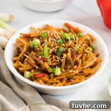 Bowl of vegan lo mein noodles topped with green onion and sesame seeds.