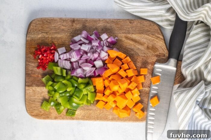 Hearty Sweet Potato Quinoa Skillet 4 Chopped chili, sweet potato, bell pepper and red onion on a cutting board with a knife.