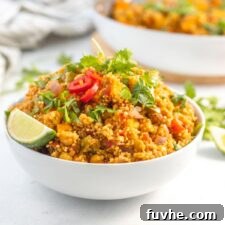 Large bowl of curried quinoa with chickpeas and sweet potato topped with sliced chilis and cilantro.