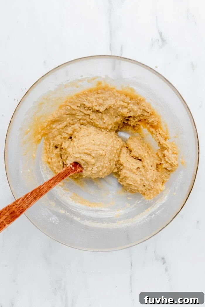 Raw crumble batter in a glass mixing bowl, appearing wet and uniform after adding liquid ingredients.