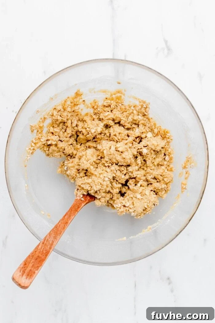 The crumble mixture now includes rolled oats, creating a rustic texture in the glass mixing bowl.