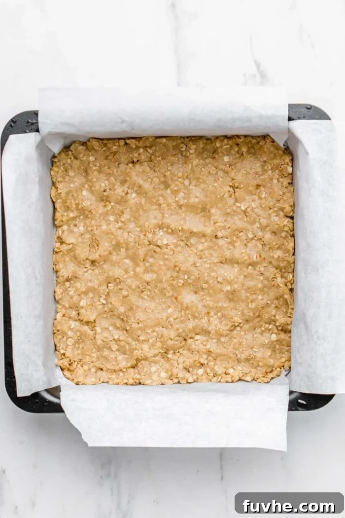 Half of the crumble mixture pressed firmly into the bottom of a baking pan, forming the crust.