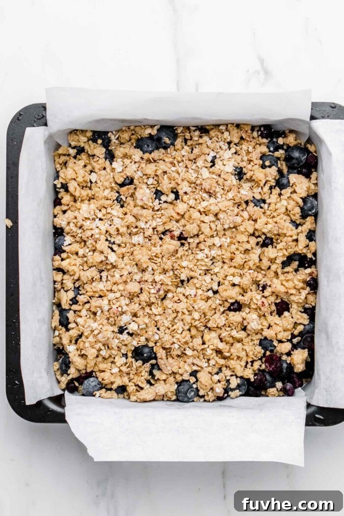 The baking pan layered with the crumble base, followed by the blueberry filling, and topped with the remaining crumble.