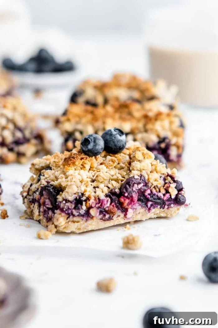 A single perfectly cut blueberry crumble oat bar resting on a piece of parchment paper, ready to be enjoyed.