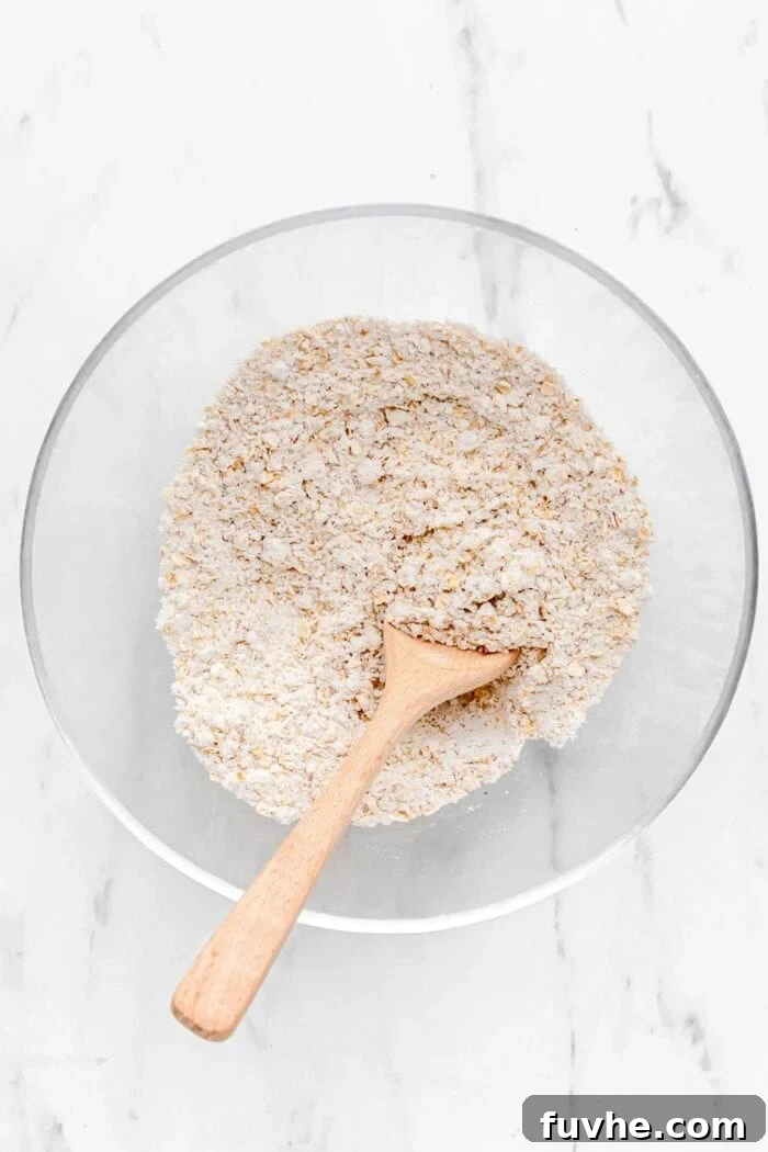 Dry baking ingredients mixed together in a mixing bowl with a wooden spoon.
