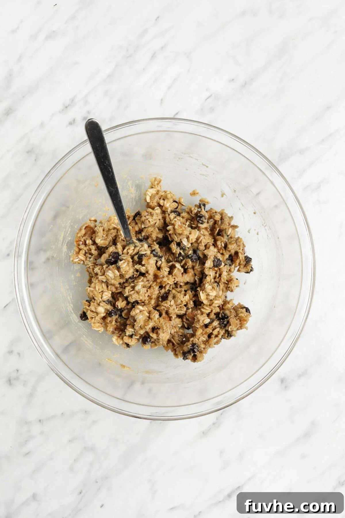Chocolate chip cookie dough in a glass mixing bowl with a spoon, showing the thick, well-combined texture.