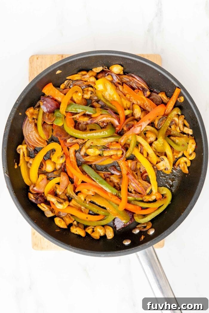 A close-up shot of perfectly cooked, colorful fajita vegetables—bell peppers, onions, and mushrooms—sizzling in a large cast iron skillet, showcasing their tender texture and slight char.