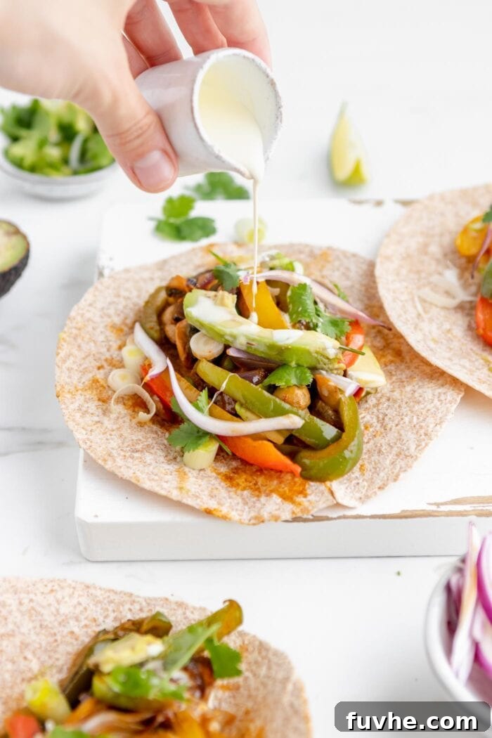 A hand gently drizzling a rich, creamy cashew cream over a freshly assembled vegan fajita, adding the perfect finishing touch to the vibrant vegetable filling.