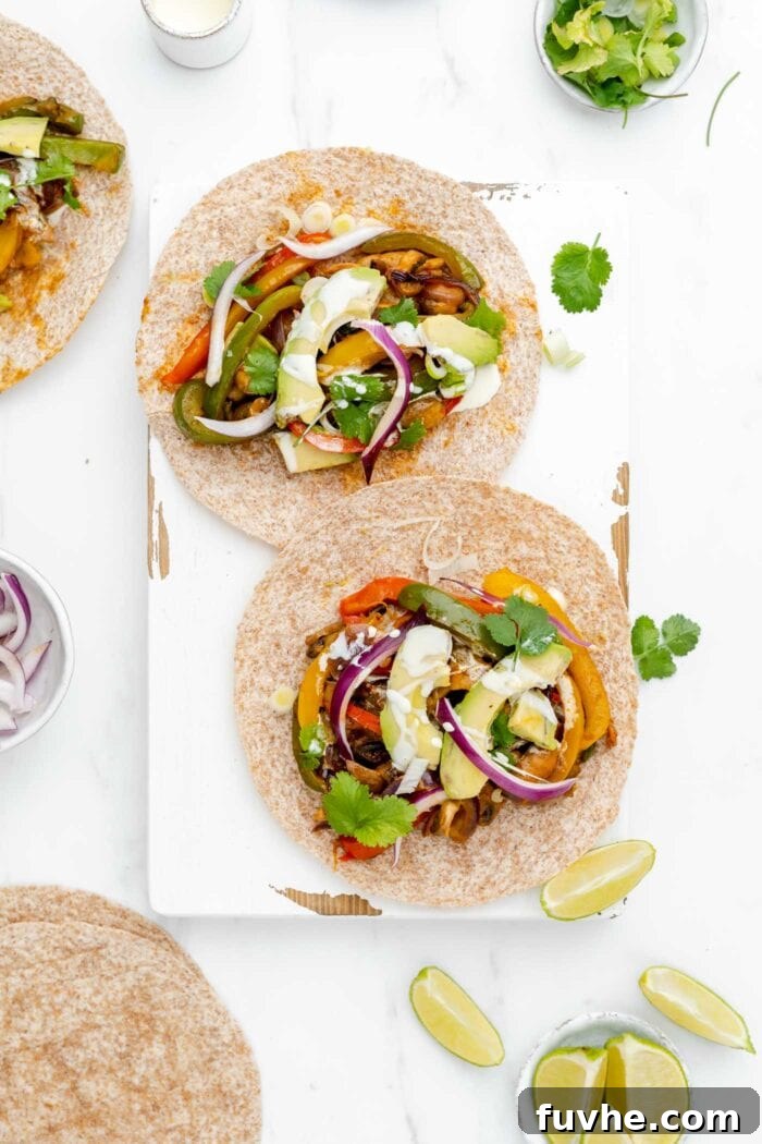 An overhead view of two beautifully assembled vegetable fajitas, garnished with fresh cilantro and a lime wedge, placed side-by-side on a light surface, ready to be served.