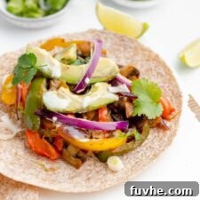 A perfectly prepared tortilla filled with colorful bell peppers, tender onions, and creamy avocado slices, presented on a rustic cutting board.