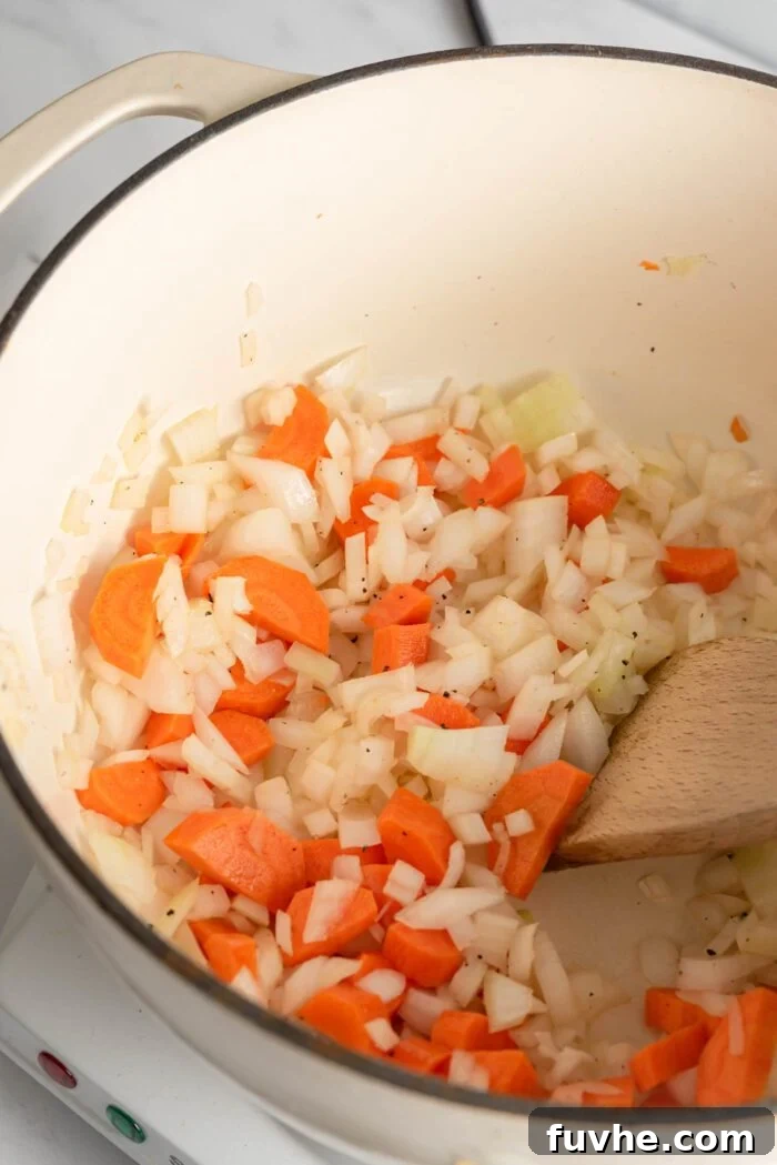 Sautéed onion, garlic and carrot in a large soup pot with a wooden spoon.