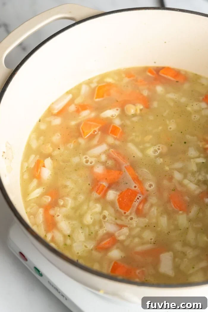 Brothy orzo chickpea lemon soup cooking in a large soup pot.