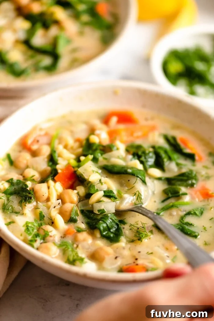 Lifting a spoonful of lemon chickpea orzo soup from a bowl.