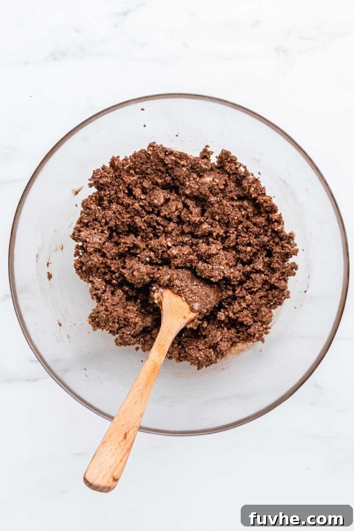 A crumbly chocolate mixture, perfect for the pie crust, in a bowl with a wooden spoon ready to mix.
