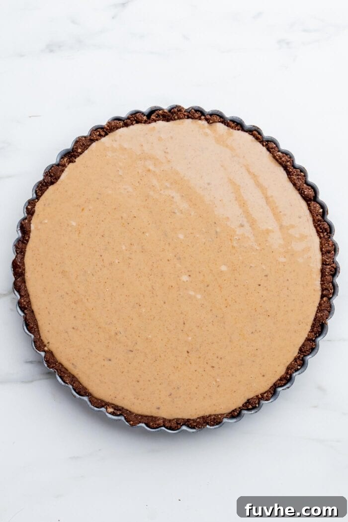 Overhead view of an unadorned peanut butter pie with a dark chocolate crust, looking smooth and ready for chilling.