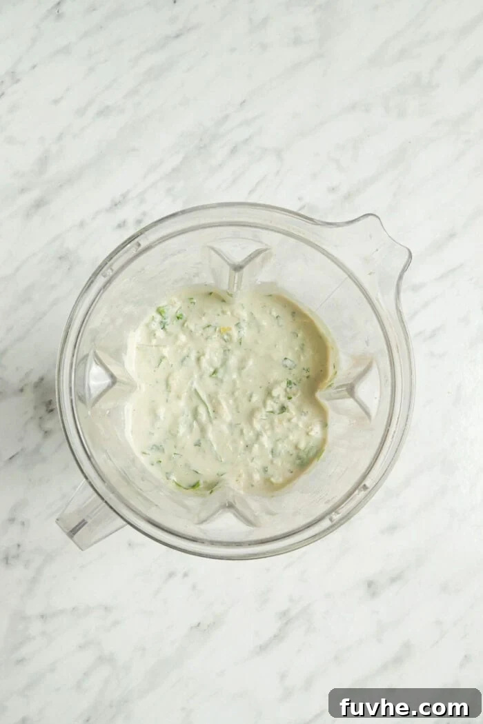 Velvety Vegan Spinach Artichoke Dip 6 A creamy mixture with spinach in it in a blender container.
