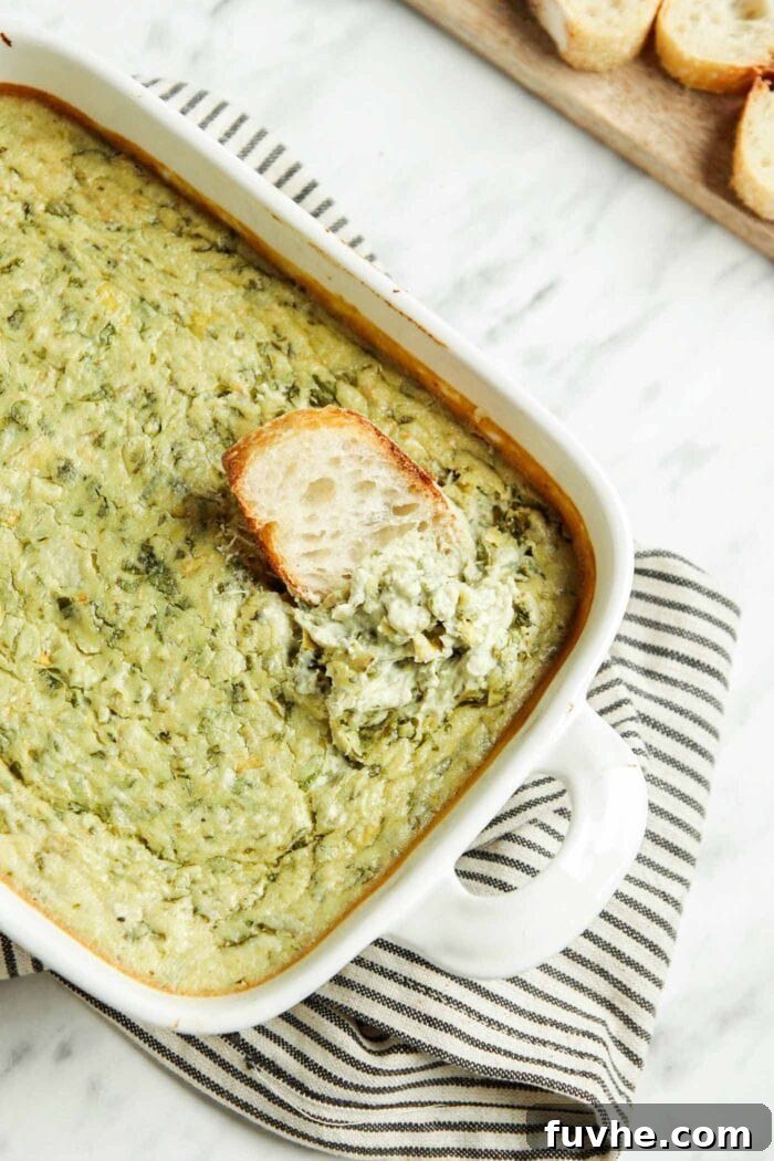 Velvety Vegan Spinach Artichoke Dip 8 Dipping some bread into a baking dish of spinach artichoke dip.