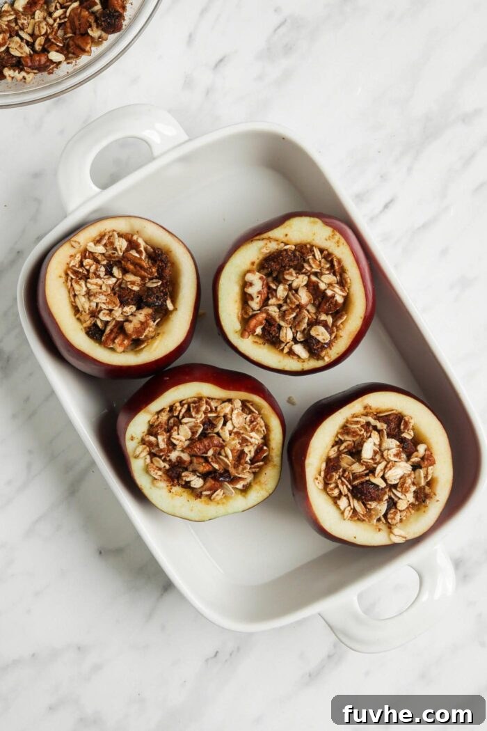 Wholesome Vegan Stuffed Apples 7 Four beautifully stuffed apples arranged in a baking dish with a shallow layer of water at the bottom.