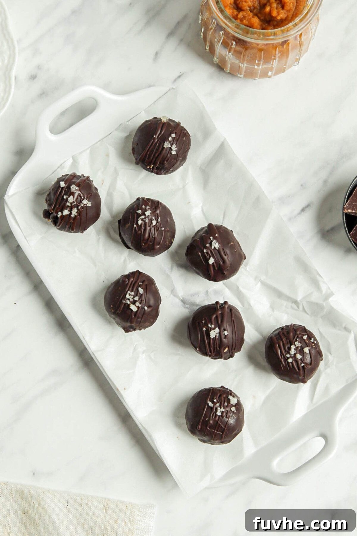 Spiced Vegan Pumpkin Chocolate Truffles 6 Chocolate pumpkin balls on a parchment paper-lined tray.