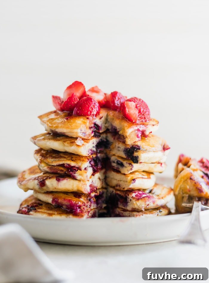 A slice taken from a stack of berry banana pancakes, topped with diced strawberries and a fork on the plate.