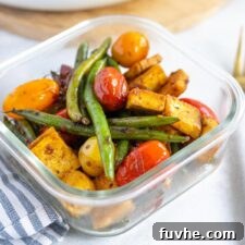 Tofu, tomatoes, green beans, and onions are packed into a clear glass storage container for meal prep.