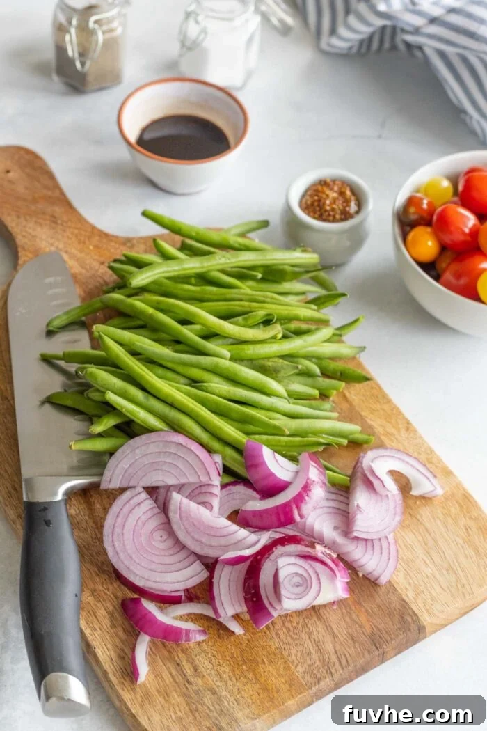Freshly chopped onions and trimmed green beans neatly arranged on a cutting board, ready for cooking.