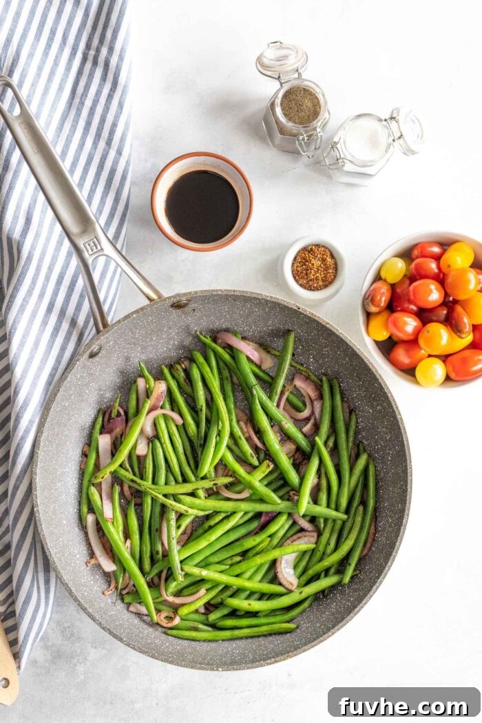 Green beans and sliced onions gently cooking in a skillet, softening and becoming fragrant.