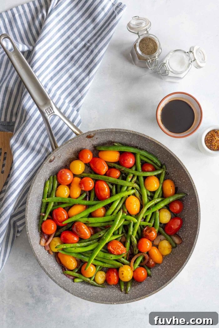 A vibrant mix of green beans, onions, and cherry tomatoes sautéing together in a skillet, creating a colorful and aromatic base.