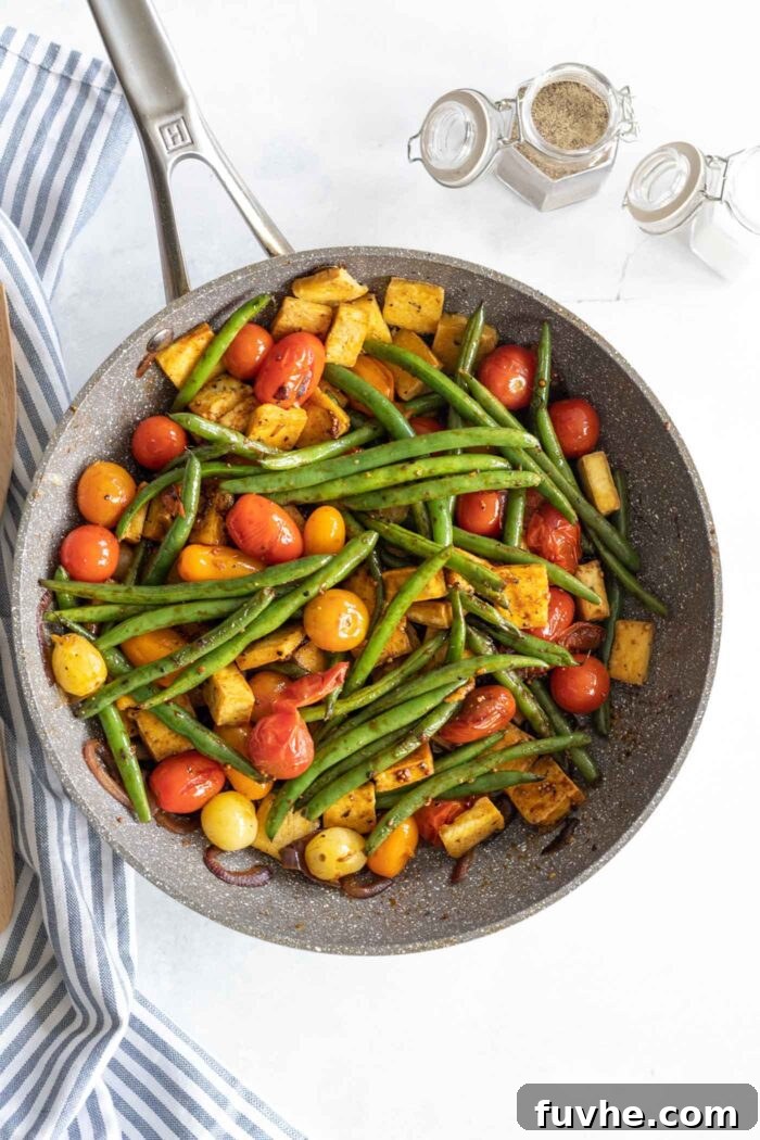 A non-stick pan filled with golden-brown tofu cubes, vibrant green beans, cherry tomatoes, and red onion, all coated in a glossy balsamic glaze.