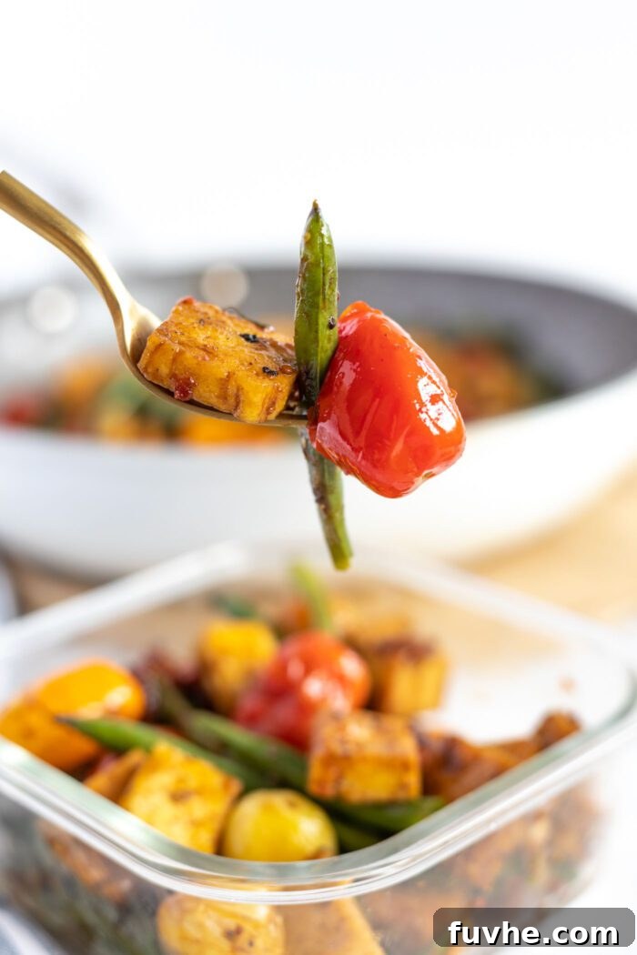 A fork holding a piece of balsamic tofu, a cherry tomato, and a green bean, showcasing the delicious components of the dish.