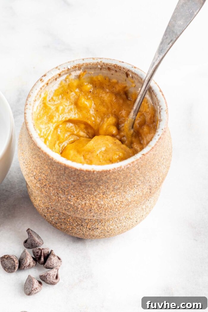 Mixed pumpkin batter in a mug with a spoon.