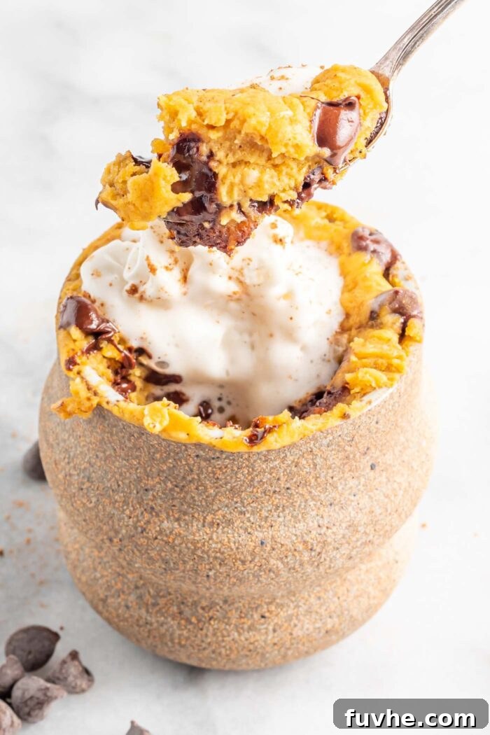 Spoonful of pumpkin chocolate chip mug cake over a mug of cake topped with whipped cream.