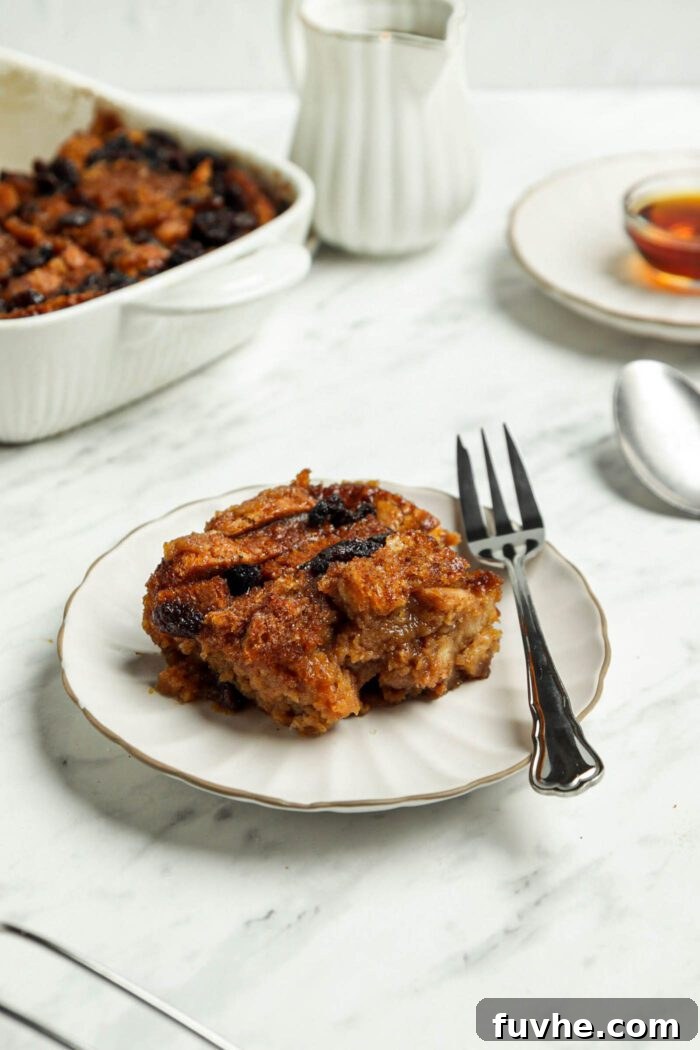 A perfectly portioned square of vegan raisin bread pudding served on a white plate with a fork, ready to be eaten.